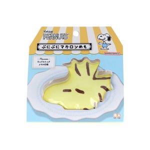 May include: A package featuring a yellow, cartoon-style macaron-shaped notepad with brown accents, resembling a character from Peanuts. The packaging includes Japanese text and a Snoopy illustration. The notepad is on a white plate.