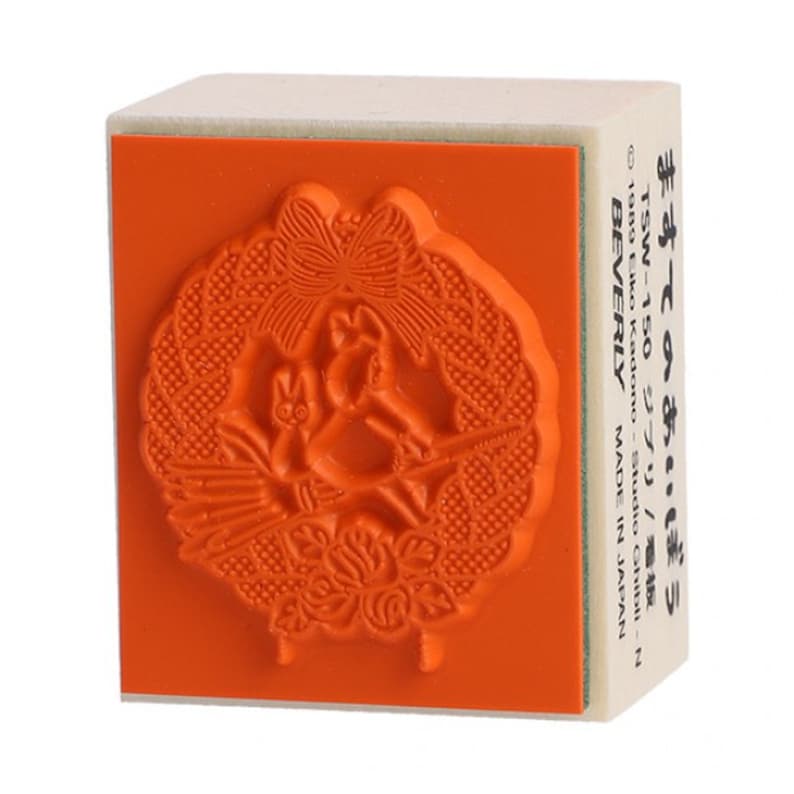 May include: A wooden stamp with an orange rubber surface featuring a detailed design of a bird in a wreath with a butterfly. The text "ますてのあい・ぼう TSW-150 ジブリ/板 1989 Eiko Kadono - Studio Ghibli-N BEVERLY MADE IN JAPAN" is printed on the side of the stamp.