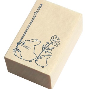May include: Wooden stamp with a blue line drawing of two rabbits. One rabbit is holding a stick and the other is holding a flower.