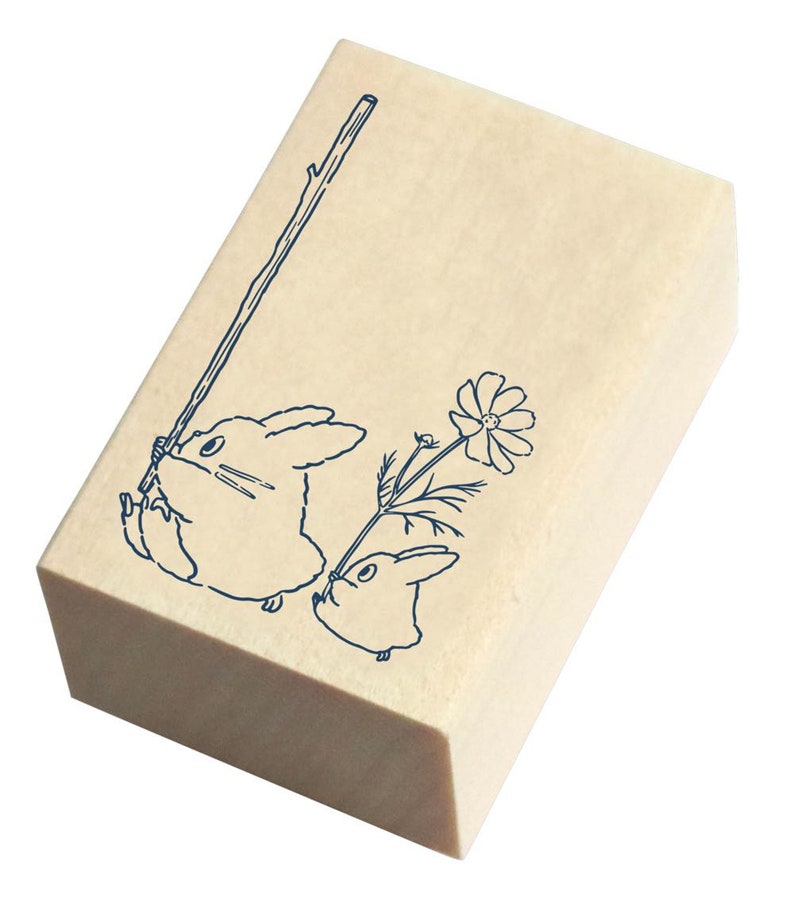 May include: Wooden stamp with a blue line drawing of two rabbits. One rabbit is holding a stick and the other is holding a flower.