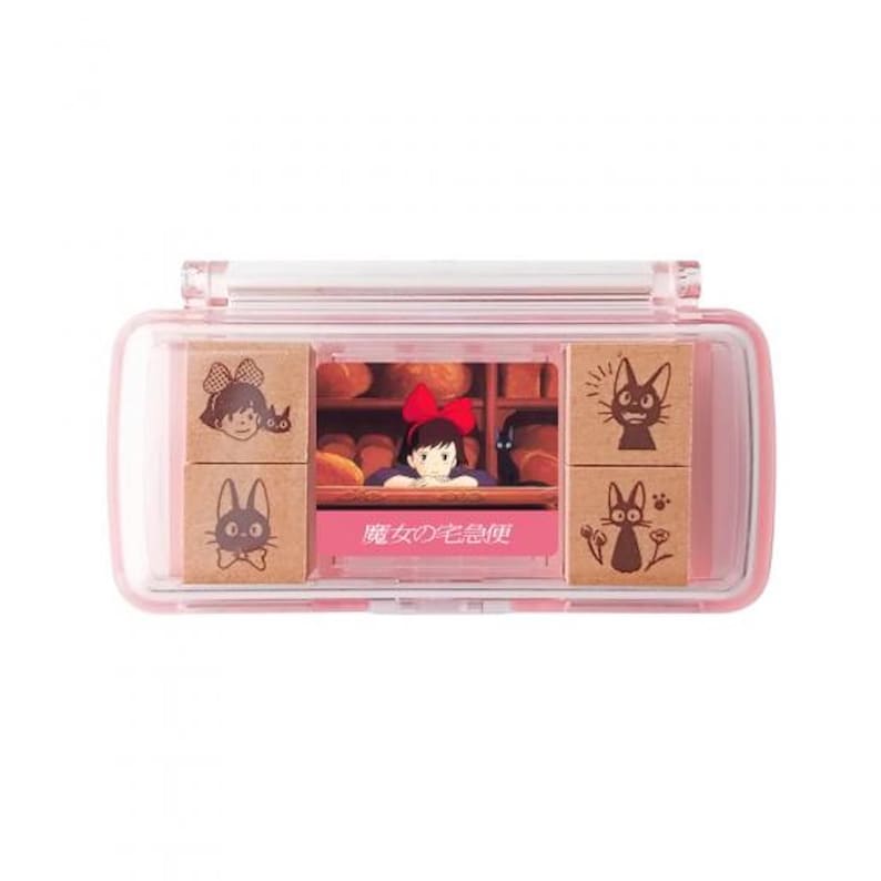 May include: A pink plastic case with a clear lid containing six wooden stamps featuring characters from the movie Kiki's Delivery Service. The stamps feature Kiki, Jiji, and a scene from the bakery. The case has the text "魔女の宅急便" printed on the front.