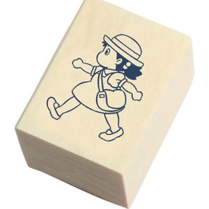 May include: A wooden rubber stamp with a blue line drawing of a girl wearing a hat and carrying a bag. The girl is walking to the right.