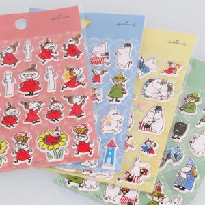 May include: Four sheets of colorful stickers featuring characters from the Moomin series. The stickers are on a white background with the Hallmark logo in the top right corner of each sheet. The stickers are of various sizes and shapes, and feature Moomin characters such as Moominmamma, Moominpappa, and Sniff.