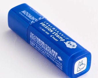 Puede incluir: Sellos de tinta azul y blanco con un personaje de Moomin y el texto "FRIXION stamp" y "こすると消えるスタンプ" en japonés. El sello está hecho por Pilot y Sun-Star.