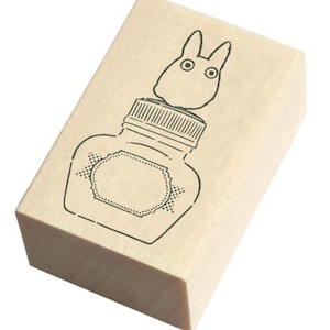 May include: A wooden stamp with a black and white illustration of a bottle with a lid and a cartoon creature on top of the lid.