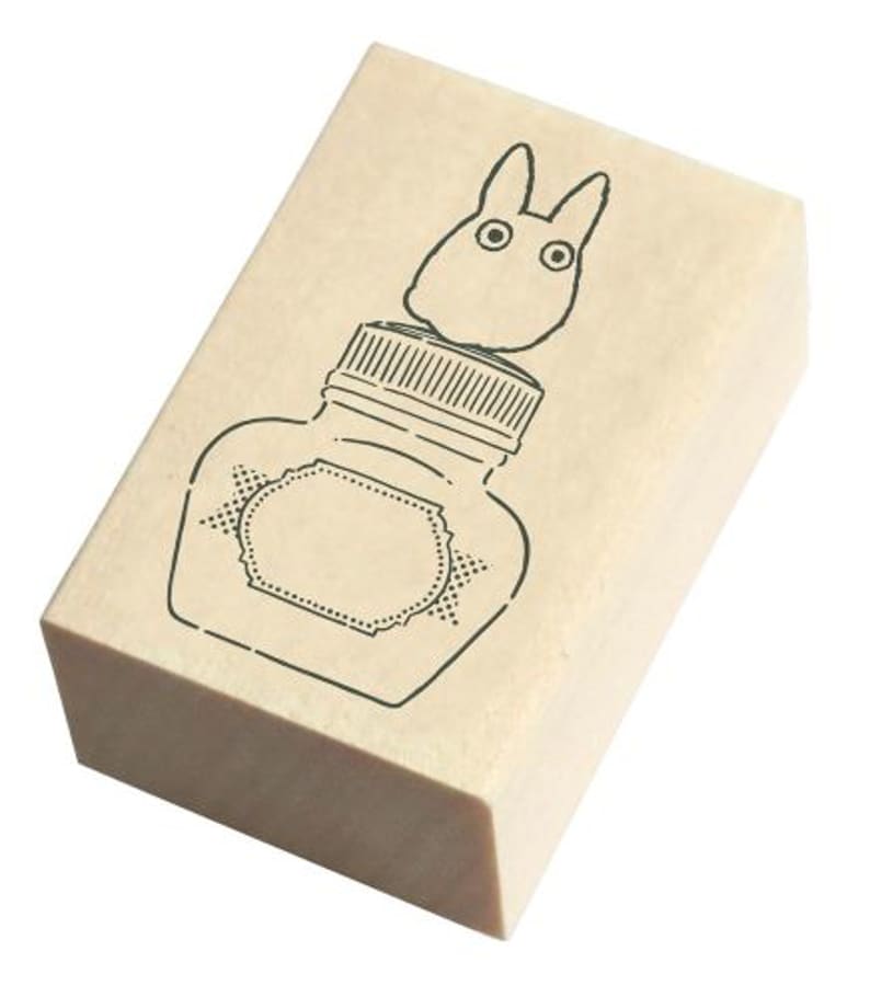 May include: A wooden stamp with a black and white illustration of a bottle with a lid and a cartoon creature on top of the lid.