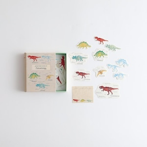 May include: A set of colourful dinosaur stickers in a small box. The stickers feature different dinosaurs, including a Tyrannosaurus Rex, a Stegosaurus, and a Triceratops. The box has the text "picture book stickers of Paleontology" on the front.