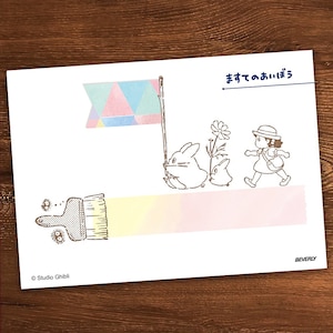 May include: A white card with a brown line drawing of a girl walking with two furry creatures. The girl is wearing a hat and carrying a bag. The creatures are holding a flag with a colorful triangle pattern. The text "まってたのしぼう" is written in Japanese at the top of the card. The text "Studio Ghibli" is at the bottom of the card.