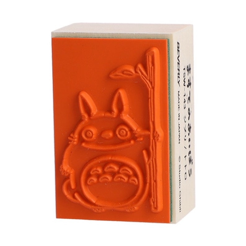 May include: Orange rubber stamp with a cartoon image of Totoro from the Studio Ghibli film My Neighbor Totoro. The stamp is on a wooden block with the text "TSW-143 ジブリ/トト0 BEVERLY MADE IN JAPAN Studio Ghibli" printed on the side.