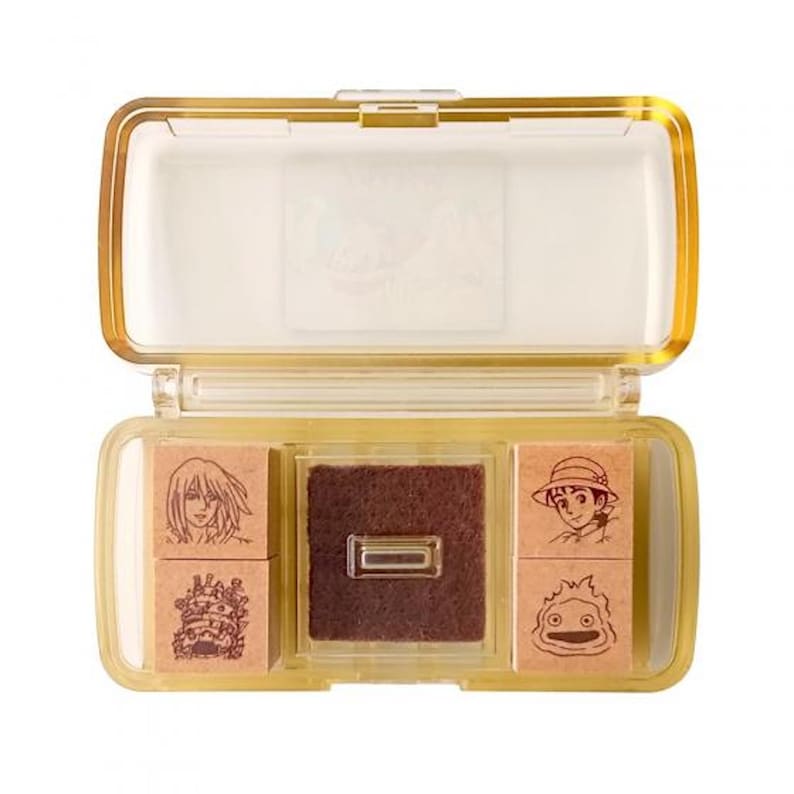 May include: A clear plastic case with a brown foam pad and four wooden stamps featuring characters from the animated film "Howl's Moving Castle".