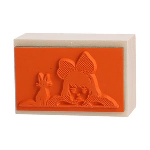 May include: A wooden stamp with an orange rubber surface. The design on the stamp is a girl with a bow in her hair and a cat beside her.