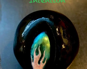 May include: Black sphere with a green and blue flame design. The sphere is black with a glossy finish. The text "Black Hole Seed of Intention" is written in green above the sphere.