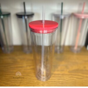 以下が含まれることがあります： 赤い蓋とストローが付いた透明なプラスチック製のタンブラー。タンブラーは空で、表面がテクスチャ加工されています。タンブラーは木製の表面の上に置かれています。