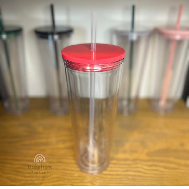 以下が含まれることがあります： 赤い蓋とストローが付いた透明なプラスチック製のタンブラー。タンブラーは空で、表面がテクスチャ加工されています。タンブラーは木製の表面の上に置かれています。