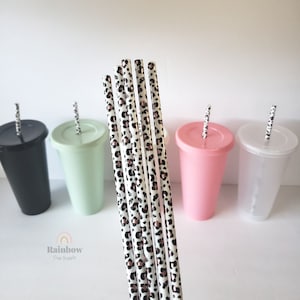 May include: Set of six reusable straws with a leopard print and rose gold accents. The straws are shown in front of four tumblers in black, green, pink, and clear.