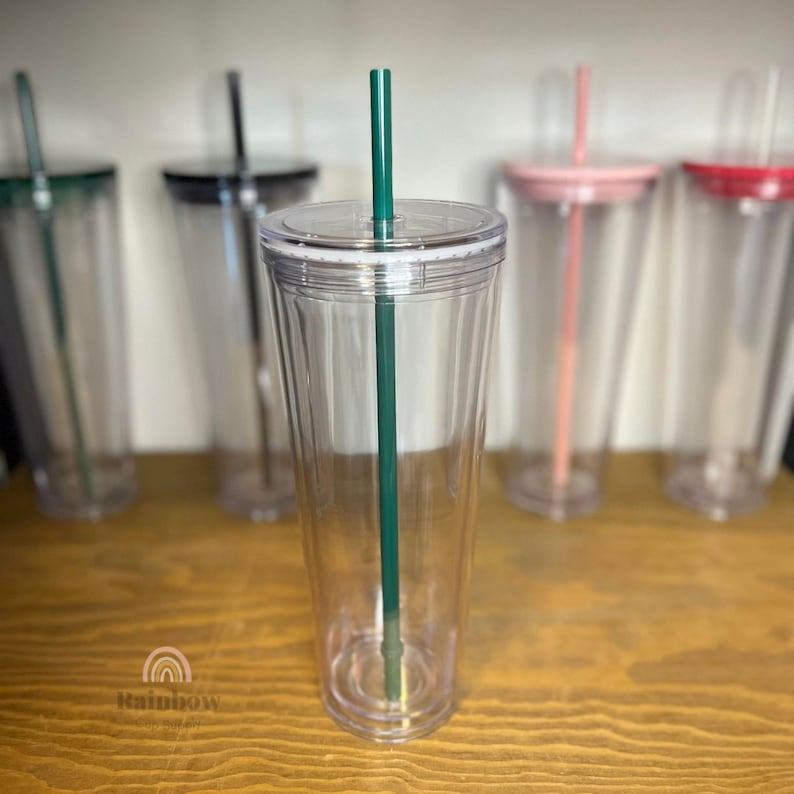 以下が含まれることがあります： 緑のストローが付いた透明なプラスチック製のタンブラー。タンブラーは空で、白い蓋が付いています。