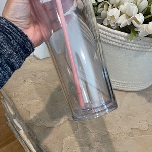 以下が含まれることがあります： ピンクの蓋とピンクのストローが付いた透明なプラスチック製のタンブラー。タンブラーは空で、二重壁になっています。