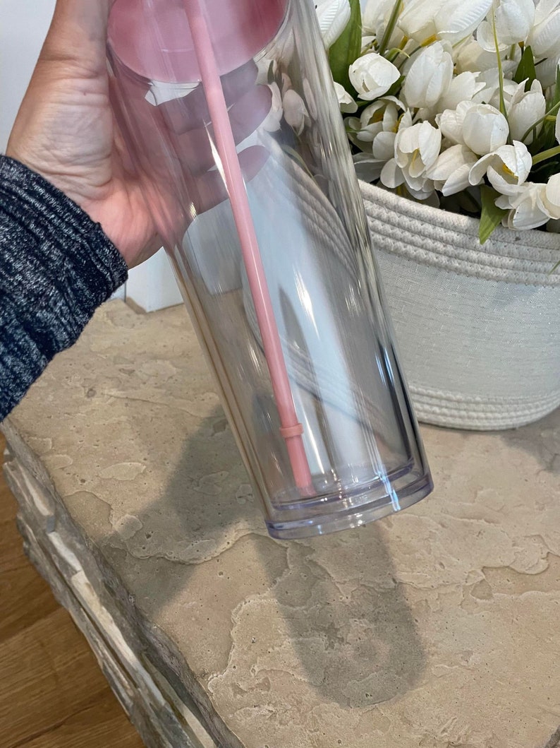 以下が含まれることがあります： ピンクの蓋とピンクのストローが付いた透明なプラスチック製のタンブラー。タンブラーは空で、二重壁になっています。
