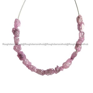May include: A strand of rough, uncut pink gemstones, strung on a thin wire. The gemstones have a natural, irregular shape and a soft, light pink hue. The image is set against a white background.