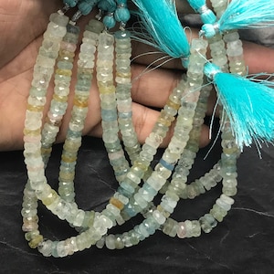 May include: A strand of light blue aquamarine beads with a faceted, barrel shape. The beads are strung on a thin cord and have a subtle shimmer.
