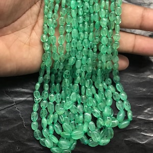 May include: A strand of green emerald gemstone beads. The beads are oval shaped and have a smooth, polished finish.