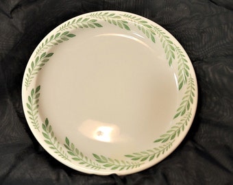 May include: A white ceramic dinner plate with a green leafy design around the rim.