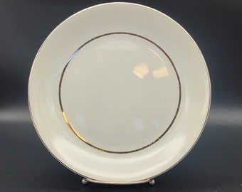 Puede incluir: Un plato de cena de cerámica blanca con una fina banda dorada alrededor del borde.