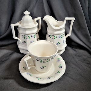 May include: A white tea set with a floral pattern in shades of blue, green, and pink. The set includes a teapot, creamer, and a cup and saucer.