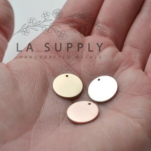 Op de afbeelding: Drie ronde metalen schijven met een gat aan de bovenkant. De schijven zijn goud, zilver en ros&eacute; goud.