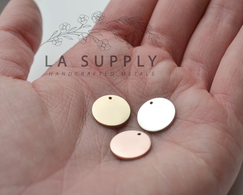 Op de afbeelding: Drie ronde metalen schijven met een gat aan de bovenkant. De schijven zijn goud, zilver en ros&eacute; goud.