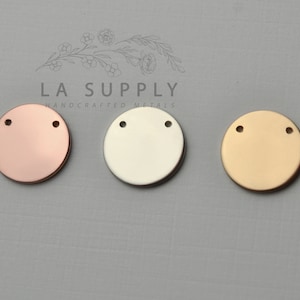 Op de afbeelding: Drie ronde metalen schijven met elk twee gaten. De schijven zijn in ros&eacute; goud, zilver en goud.