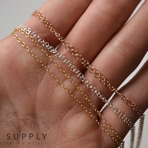 May include: Three different chain necklaces in gold, silver, and rose gold. The chains are laid out on a hand, with the gold chain on top, followed by the silver chain, and then the rose gold chain.