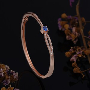 May include: A rose gold bangle bracelet with a blue gemstone and clear cubic zirconia stones.