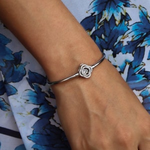 May include: A silver bangle bracelet with a rose-shaped charm set with clear cubic zirconia stones.