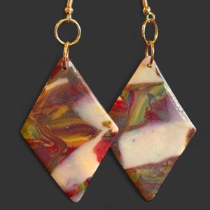 May include: A pair of diamond-shaped earrings featuring a marbled pattern of red, yellow, green, and white colors. The earrings are suspended from gold-toned metal hooks attached to circular jump rings, creating a dangling design with a smooth finish.