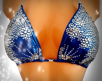 May include: A blue bikini top with silver embellishments. The triangle cups are adorned with clusters of silver stones and a central floral design. The straps and the clasp are also embellished with silver stones.