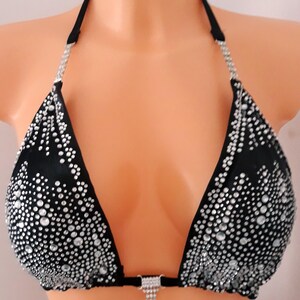 May include: Black bikini top with sparkling rhinestone embellishments. The triangle cups are densely covered with clear rhinestones, creating a shimmering effect. The straps and trim are black, with a small rhinestone pendant at the center.