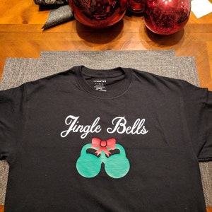 May include: Black t-shirt with a white graphic of jingle bells with a red bow. The graphic is of two green bells with a red bow on top.