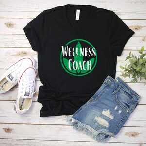 May include: Black v-neck t-shirt with a green leaf design and the text "Wellness Coach".