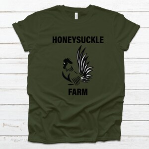 Pu&ograve; includere: Una maglietta verde con un grafico di gallo nero e il testo "Honeysuckle Farm".