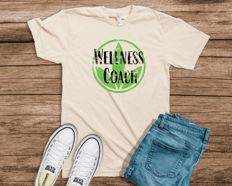 May include: A beige t-shirt with a black and green graphic that says "Wellness Coach".
