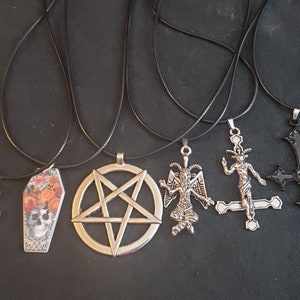 May include: Five black cord necklaces with different silver pendants. The pendants include a pentagram, a coffin with floral accents, a snake, a devil figure, and a crucifix.