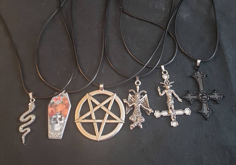 May include: Five black cord necklaces with different silver pendants. The pendants include a pentagram, a coffin with floral accents, a snake, a devil figure, and a crucifix.