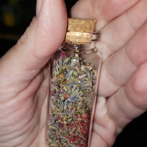 May include: A small glass bottle with a cork stopper filled with dried lavender, rose petals, and red glitter.
