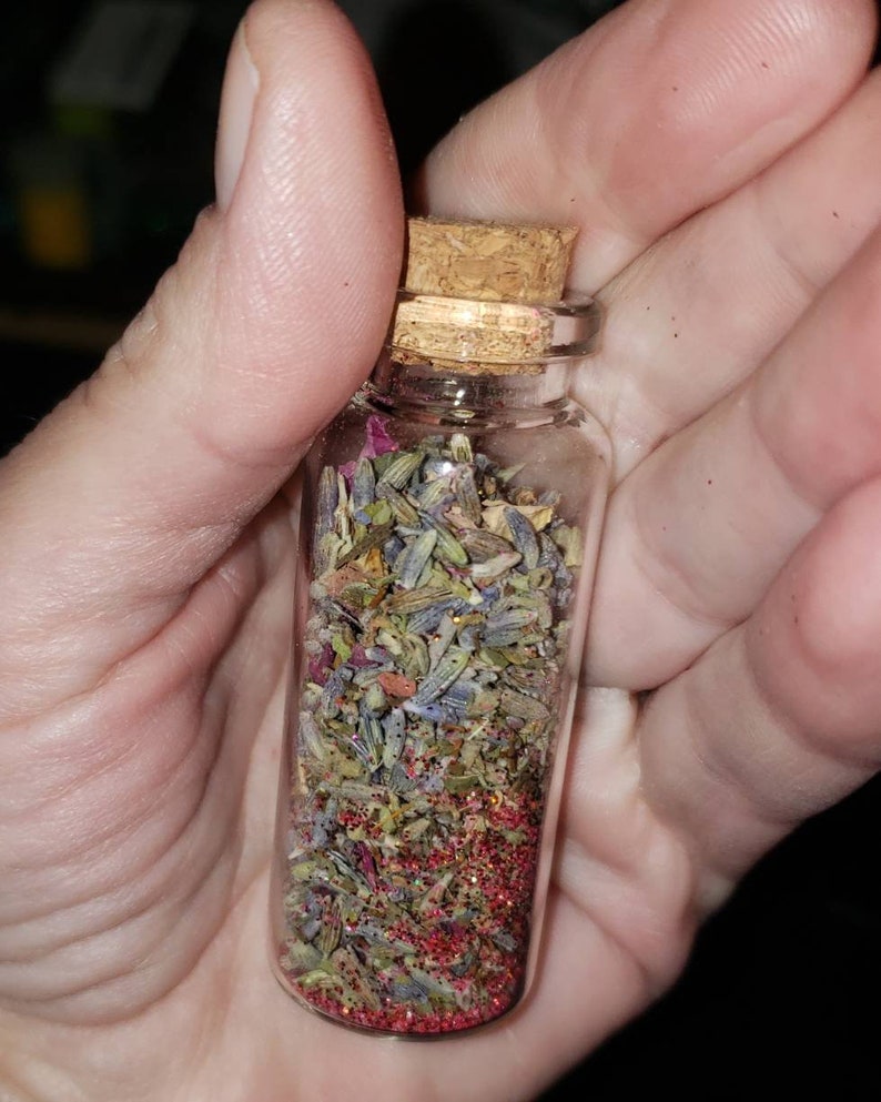 May include: A small glass bottle with a cork stopper filled with dried lavender, rose petals, and red glitter.
