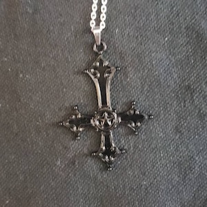 May include: A black metal cross pendant with a five-pointed star in the center, hanging from a silver chain.