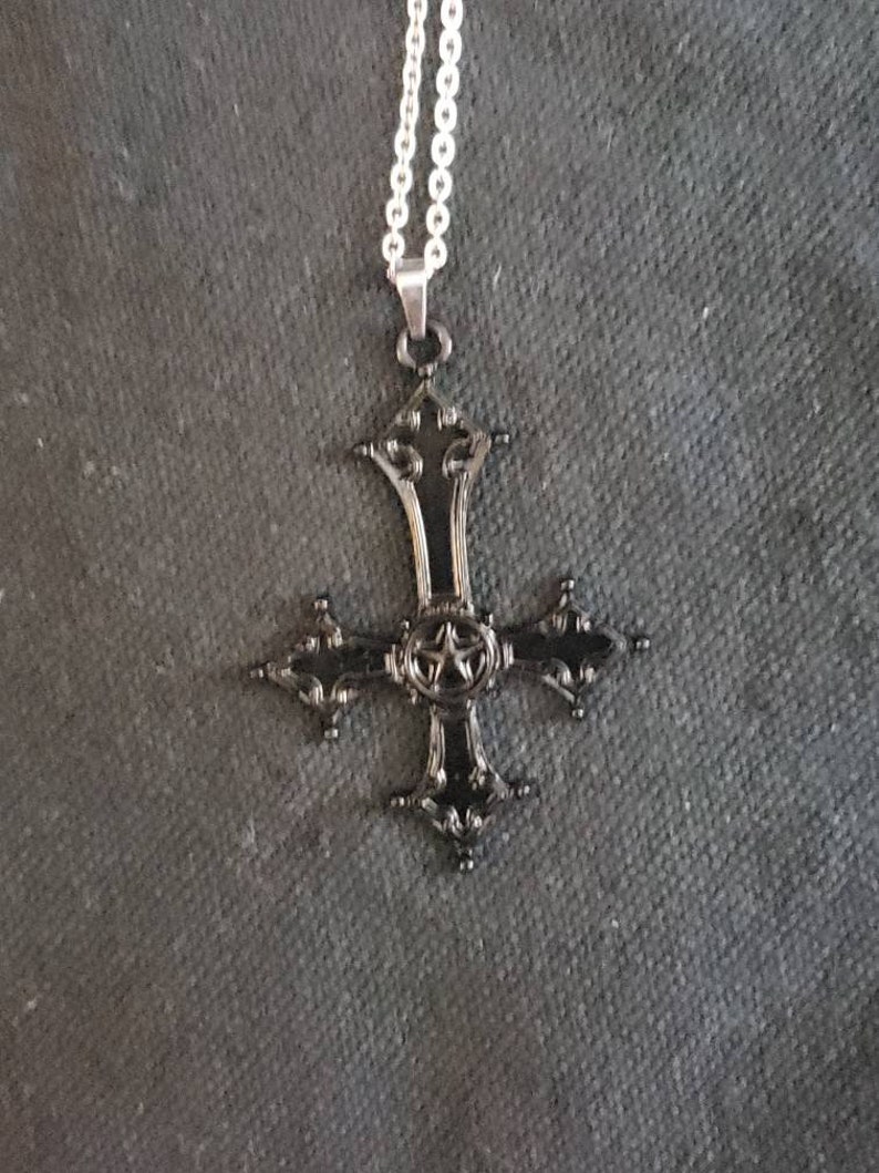 May include: A black metal cross pendant with a five-pointed star in the center, hanging from a silver chain.