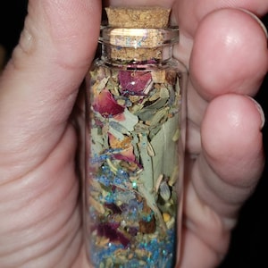 May include: A small glass bottle with a cork stopper filled with dried herbs, flowers, and blue glitter.