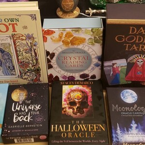 May include: A collection of tarot and oracle decks, including "Color Your Own Tarot", "The Healing Oracle Crystal Reading Cards", "Dark Goddess Tarot", "The Healing Mantra Deck", "The Universe Has Your Back", "The Halloween Oracle", and "Moonology Oracle Cards".