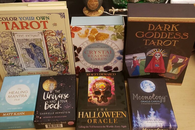 May include: A collection of tarot and oracle decks, including "Color Your Own Tarot", "The Healing Oracle Crystal Reading Cards", "Dark Goddess Tarot", "The Healing Mantra Deck", "The Universe Has Your Back", "The Halloween Oracle", and "Moonology Oracle Cards".